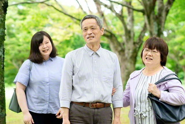 「腕を組むのなんて何年ぶりかな(笑い)。これも、病気になったおかげ」と照れ笑いする前田さん㊥を妻・英巳子さん㊨と長女・由美子さんが囲む
