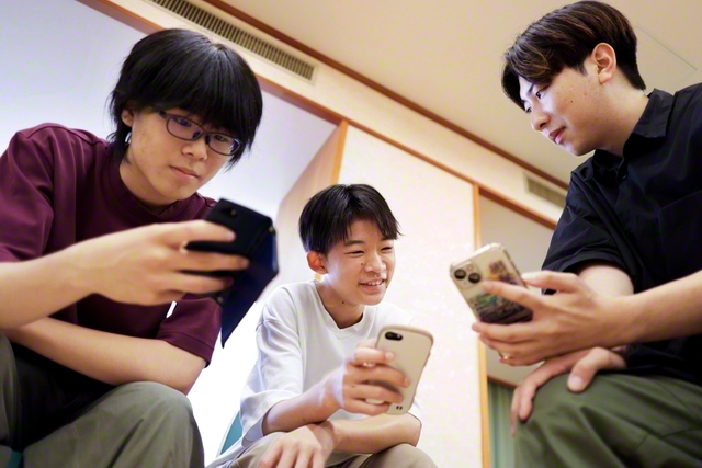 大学生のお兄さん㊨にアドバイスを受けながら、スマホで英文の作成に取り組む中等部員たち