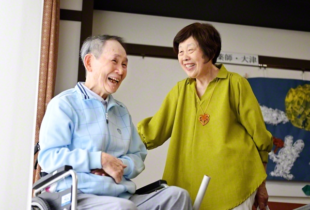 「一緒に走り切りましょう！」と夫・秀幸さん㊧を励ます伊東さん。介護が在宅でも施設でも、夫婦ともに、広布への思いは変わらない
