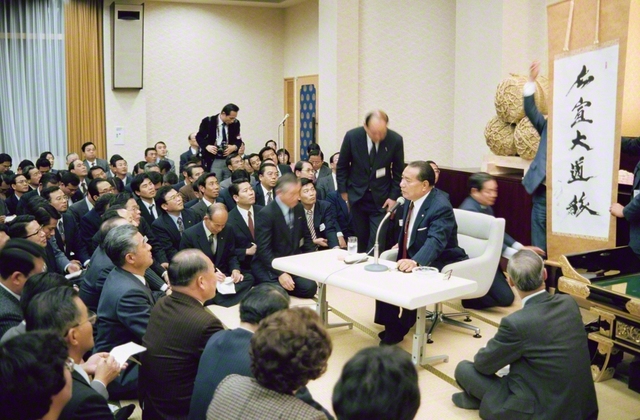 「広宣大道旅」――1983年12月14日、兵庫池田講堂（現・西宮平和講堂）での幹部会で、兵庫の友に贈った書を紹介する池田先生。この日、兵庫の“地涌の菩薩”の幸福・勝利を願って、皆で万歳三唱も行った