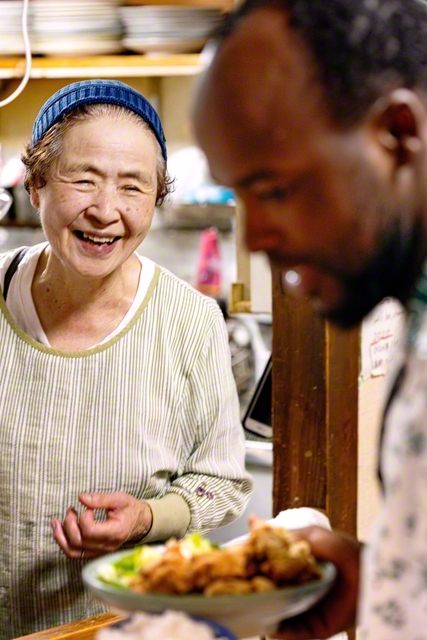キッチンから料理を渡す大森さん㊧。はじける笑顔もお裾分け