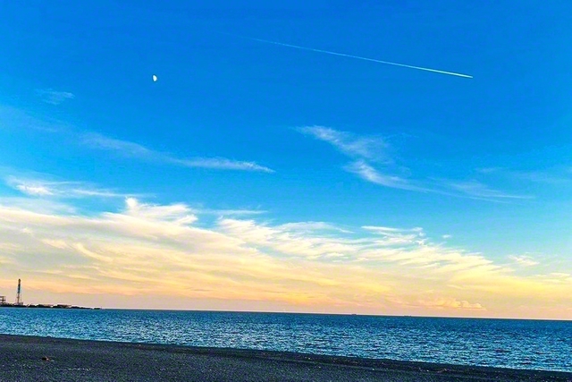 煙樹ケ浜の夕空（和歌山県美浜町）。上弦の月と飛行機雲が共演＝和歌山・木下智裕通信員