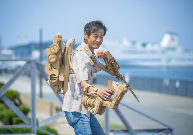 作品を身にまとった山口さんは、カメラを向けるより先に、決めポーズ。「この段ボールの断面がいいでしょ。色を塗っちゃあ、もったいないよね。ここんところを押せば、ほら変形もするし……」。話し出したら止まらない