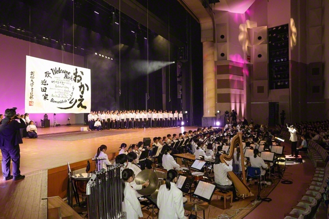 「パイオニア吹奏楽団」の演奏に合わせて有志が「桜花の縁」を合唱。「書道部」がさまざまな言語で「おかえり」を意味する言葉を力いっぱい書き上げた