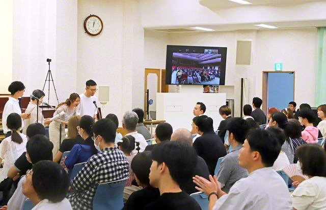 広布前進の誓いを新たにする兵庫・西宮総県とマレーシアの集い。マレーシアのチュー・オード・レイさんが信仰体験を力強く。“労苦こそ人生の宝”との池田先生の指針を胸に、起業したデザイン会社で信頼を広げ、職場の同僚が御本尊を受持した喜びを語った（西宮平和講堂で）