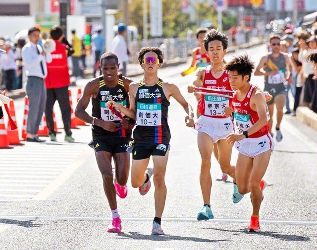 小池選手（左から2人目）が3区のムチーニ選手（左端）にタスキをつなぐ（第2中継所・ゆめタウン斐川前で）