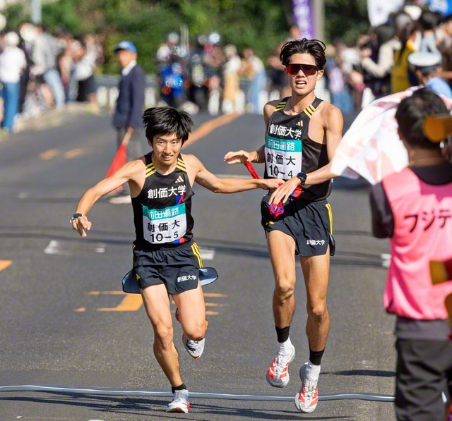 石丸選手㊨がタスキを5区の山口選手に渡す（第4中継所・鳶巣コミュニティセンター前で）