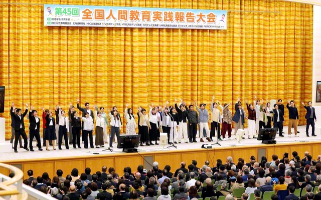 全国人間教育実践報告大会で青年教育者が合唱。小学校教諭の田中大輝さん、保育士の蘆田菜々さんが元気に司会を務めた(北海道池田講堂で)