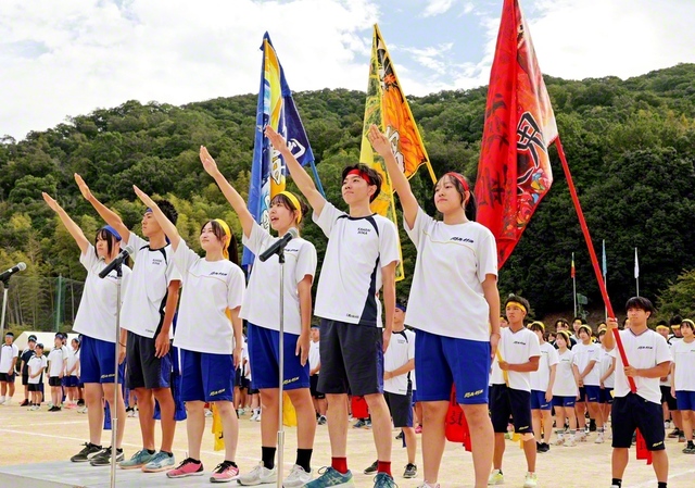 関西高の競技大会の開幕式。代表が選手宣誓を行い、赤・黄・青の梯団の旗を青空に掲げた（9月27日）