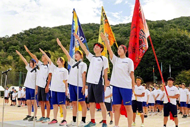 関西高の競技大会の開幕式。代表が選手宣誓を行い、赤・黄・青の梯団の旗を青空に掲げた（9月27日）