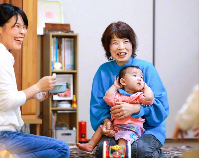 「ちょっと元気すぎて困ってるわ」と笑顔で孫の陽咲ちゃんを抱く田中さん。「池田先生への感謝と、題目の確信を受け継ぐことが人生の総仕上げ」と家族団らんの毎日を送る