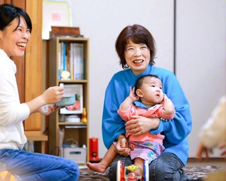 「ちょっと元気すぎて困ってるわ」と笑顔で孫の陽咲ちゃんを抱く田中さん。「池田先生への感謝と、題目の確信を受け継ぐことが人生の総仕上げ」と家族団らんの毎日を送る