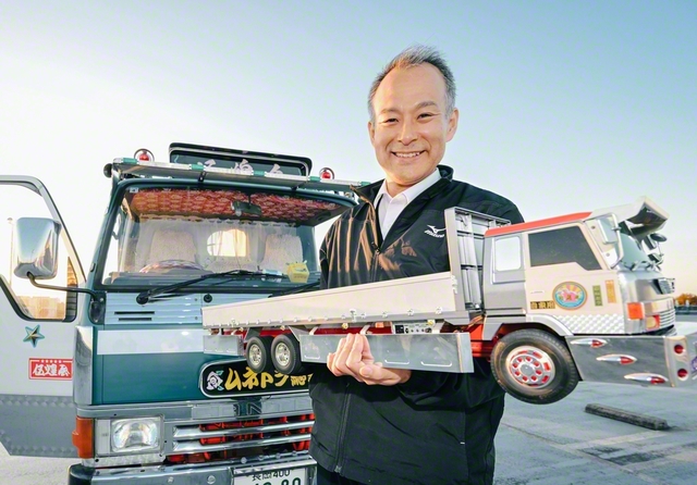 宗藤さんが腕に抱いた自作のデコトラ模型は、操縦も可能。写真後方は自家用車。もちろんデコトラである