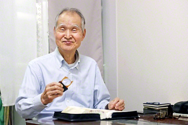 いつもテーブルの同じ場所で御書を読む佐々木さん。愛用のルーペは人生の相棒のよう