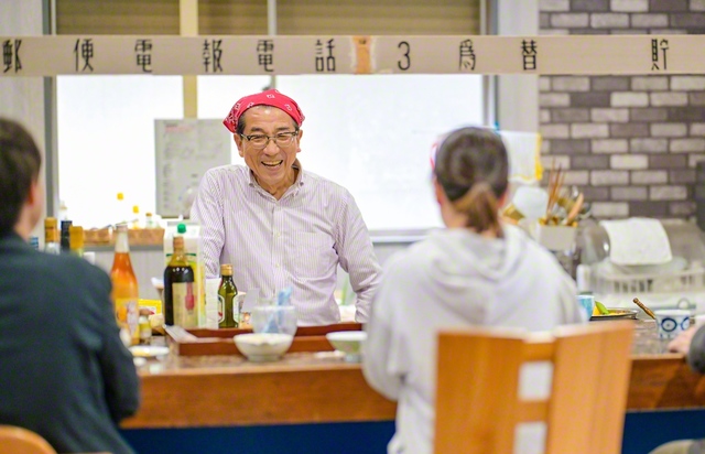 そばを振る舞う鈴木さん。「遠慮せんと、いっぱい食べてな」。「ハリー・ハウス」では郵便局の窓口にあった案内板も“再利用”し、往時の雰囲気を残す