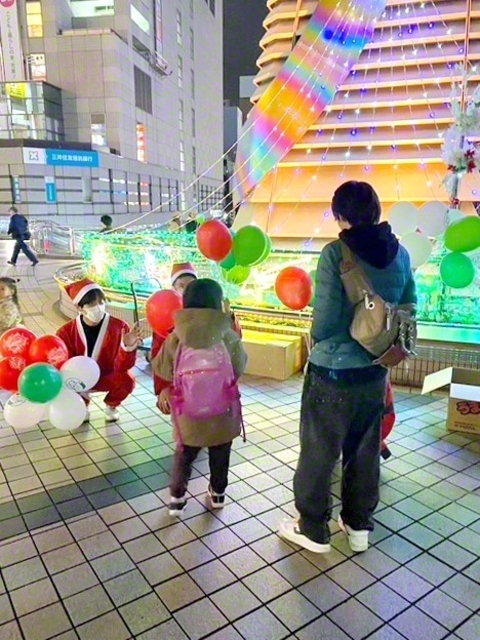 商店会のクリスマス企画。サンタに扮した創大生がしゃがんで子どもと目線を合わせ、プレゼントを渡す。その瞬間をカメラに収めたい保護者も集まる