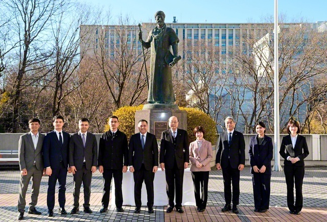 創大池田記念講堂の前庭に立つナワイー像の前で、アブドゥラフモノフ大使（左から5人目）一行が、留学生らと共に記念撮影