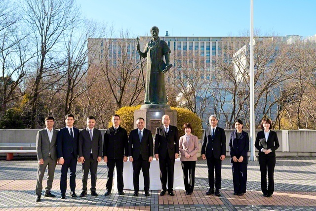 創大池田記念講堂の前庭に立つナワイー像の前で、アブドゥラフモノフ大使（左から5人目）一行が、留学生らと共に記念撮影