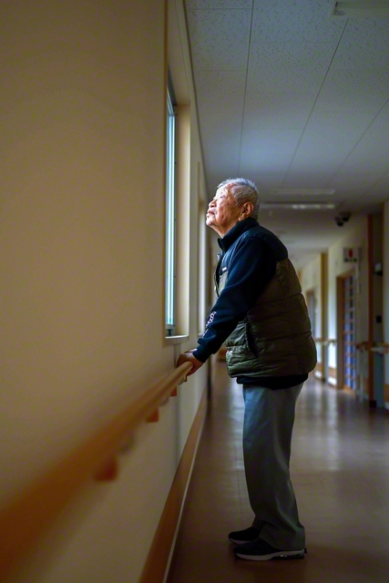 雨雲の切れ間から光が落ちる。窓辺に立つ谷口さん。そのまなざしの先に、静かな空