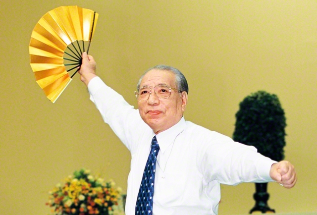 “小さくなるな！　友よ、立ち上がれ！”――本部幹部会の席上、学会歌「威風堂々の歌」の指揮を執る池田先生（2001年5月、東京戸田記念講堂で）。「無認識の壁にぶつかったとしても、『あんな人間がなんだ！』『こんな迫害がなんだ！』と笑いとばしながら、誇り高く、胸を張って生きぬいていただきたい」と