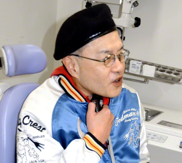 2024年に喉頭の摘出手術を受け、電気式人工喉頭で話す服部教介さん＝名古屋市の名古屋大学病院