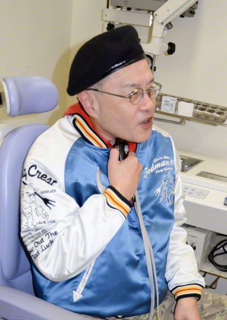 　2024年に喉頭の摘出手術を受け、電気式人工喉頭で話す服部教介さん＝名古屋市の名古屋大学病院