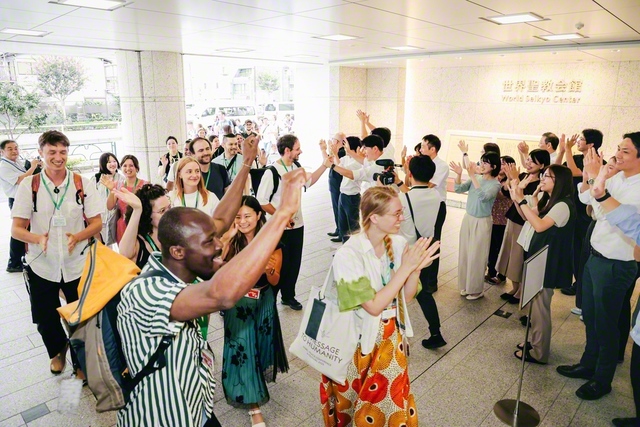 庶民が自分たちの新聞を掲げ、幸福と勝利の哲学を楽しく語り合う。民衆が新聞を手に取り団結し、社会に正義と希望の対話を広げゆく。創価の師弟の熱願が現実に（昨年、世界聖教会館を見学する海外の友）