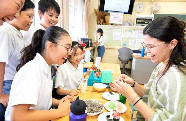 紙や毛糸で作った食べ物が並ぶ手作り屋台を囲み、笑顔で交流する児童と留学生（東京創価小学校で）