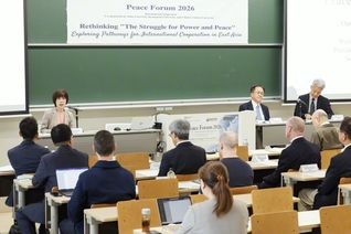 ピースフォーラムであいさつする創価大学の鈴木学長（左端）。フォーラムでは学生からも多くの質問が寄せられ、議論が交わされた（創大中央教育棟で）