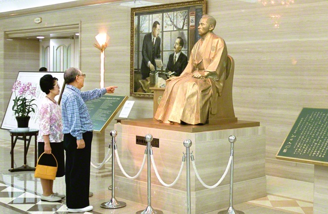 牧口先生の座像を見つめる池田先生ご夫妻（2001年7月、東京牧口記念会館で）。池田先生は牧口先生の生き方を通し、「青年とは、決して年齢ではない。心の持ち方、生き方で決まる」と