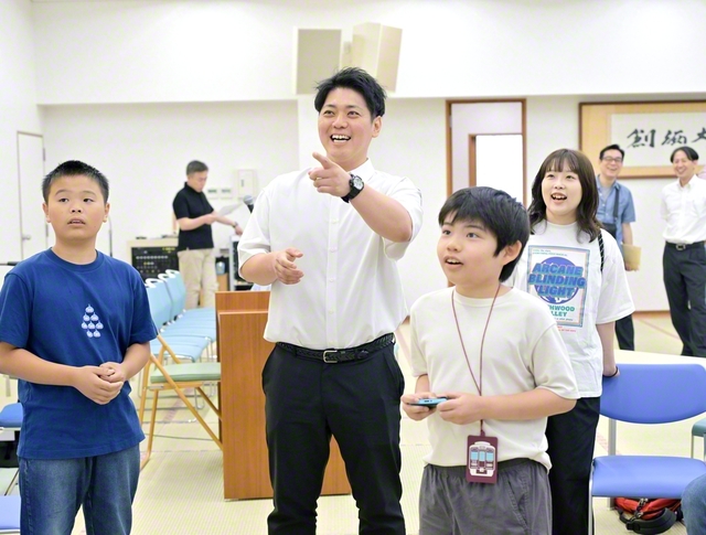 大型モニターに家庭用ゲーム機をつないで、レーシングゲームや格闘ゲームなどを一緒に楽しんでいる様子（北摂文化会館で）