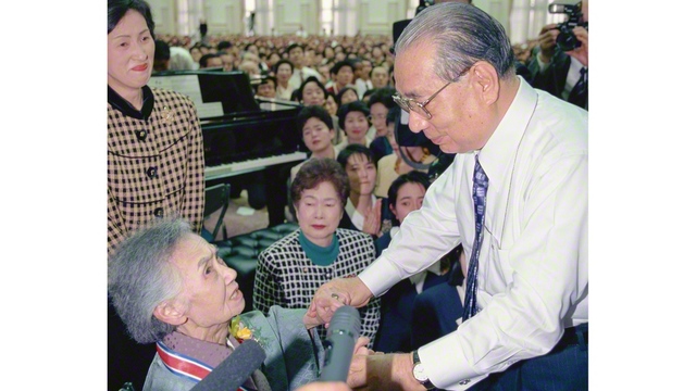 1997年2月8日に行われた本部幹部会。スピーチを終えた池田先生が、壇上から安楽花子さんが座る席へ。目が見えない安楽さんの両手を握り、「永遠に忘れません」と声をかけた（東京牧口記念会館で）