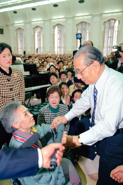 1997年2月8日に行われた本部幹部会。スピーチを終えた池田先生が、壇上から安楽花子さんが座る席へ。目が見えない安楽さんの両手を握り、「永遠に忘れません」と声をかけた（東京牧口記念会館で）