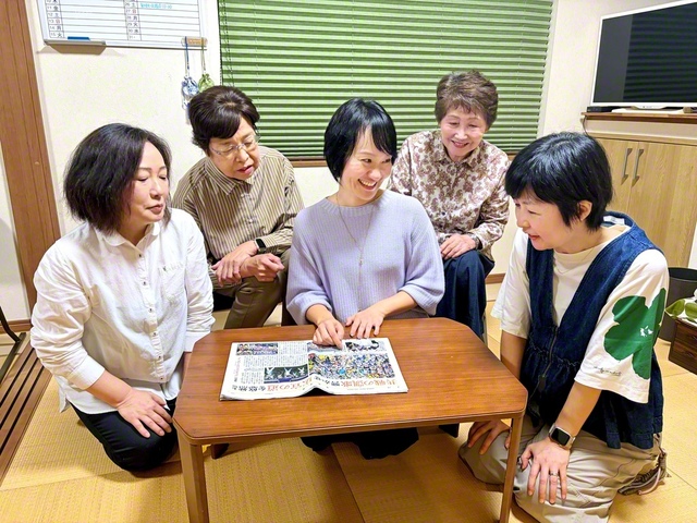 堤西地区の未来部員がたくさん写った「PEACE　PRIDE」の聖教紙面を見ながら語らう元谷さん（中央）ら。世代を超えた「総合力」で、誰もが安心して集える居場所をつくる（川崎市多摩区内で）