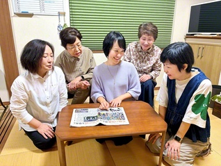 堤西地区の未来部員がたくさん写った「PEACE　PRIDE」の聖教紙面を見ながら語らう元谷さん（中央）ら。世代を超えた「総合力」で、誰もが安心して集える居場所をつくる（川崎市多摩区内で）