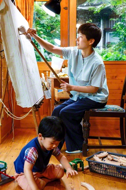 あかりさん㊨は「描く時より、絵を見て喜んでもらえる時の方がうれしい」と。一瞬の感動のために、何度も色を重ねる。おもちゃで遊ぶ長男・あおばくんの隣には、優しく、強い母がいる