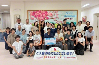ラトナーヤカさん（2列目左から6人目）の入会記念勤行会には未入会の夫も参加。先﨑女性部主任部長（同3人目）をはじめ同志が盛大に祝福した（8月）