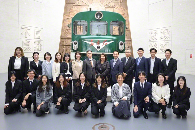 西南交通大学校史博物館の入り口に展示されているディーゼル機関車を背に、西南交通大学日本語学院の学生らと学会の訪中団が記念のカメラに