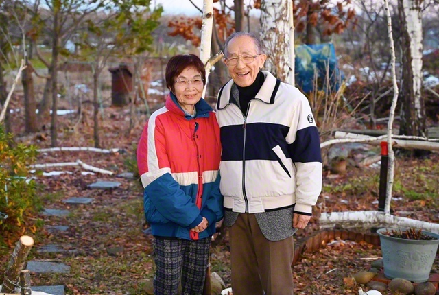 中村さん㊨と博子さんが自宅の庭で。コスモスやイチジク、八重桜やシラカバなど、転居してから花や40本の木々を植えて育ててきた。季節ごとに華やぐ様子を見ようと、地元の人も多く訪れる