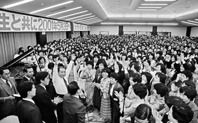 両手を高らかに挙げ、長編詩発表の場に集まった青年らに万歳で応える池田先生（1981年12月10日、大分平和会館で）。後年、この詩に曲が付けられ、学会歌「青年よ広布の山を登れ」として世界中で歌われている