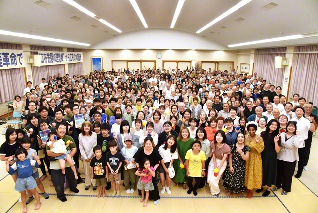 “ワン（私）”から勇気の一歩を！　桜梅桃李の青年が輝いた「ワン・ワールド・フェスティバル」。開会前には、各島で活躍する未来部員を紹介する映像企画も（奄美大島文化会館で）