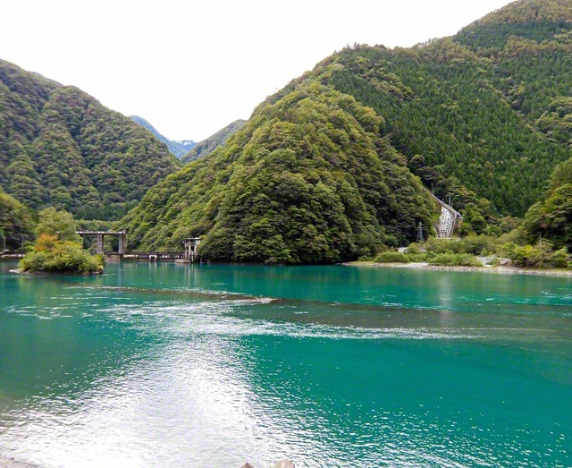 美しいエメラルドグリーンに輝く湖面。人気アニメの聖地としても知られているダム湖です。湖底には、「奈良田集落」が眠っています（杉山賢司）