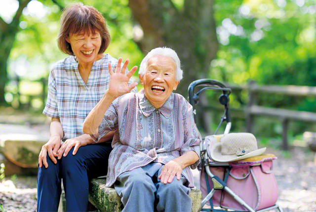 織田さん㊨が次女の森田佐智代さん（支部副女性部長〈地区女性部長兼任〉）と近くの公園へ。腰は直角に曲がっても、耳は遠くなっても、元気いっぱい。愛用の手押し車でトコトコと歩いていく。“今は亡き長女や夫の分まで、命ある限り、自分らしく広布のために”――織田さんは、そう誓っている
