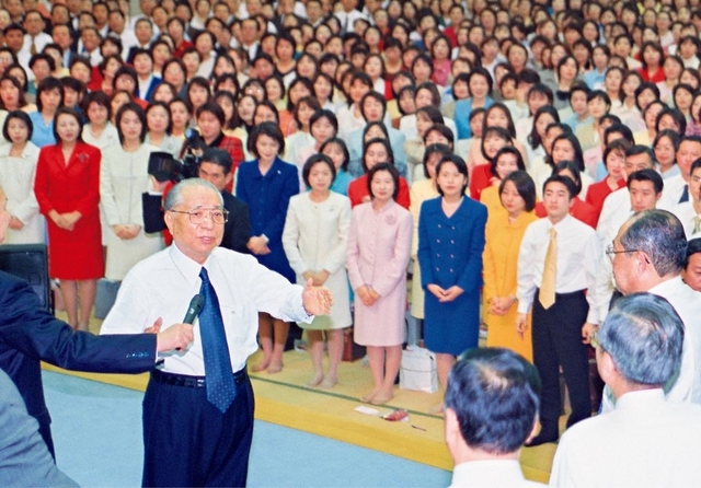 第52回「本部幹部会」で関西の同志に励ましを送る池田先生。「関西は『広宣流布の心臓部』である。関西が日本全国を、また全世界を動かしていくのである。それが関西の使命だからである」と語り、〈大関西/断固と築けり/常勝の/大城 輝き/三世に不滅と〉など3首の和歌を詠み贈った（2000年12月14日、関西戸田記念講堂）