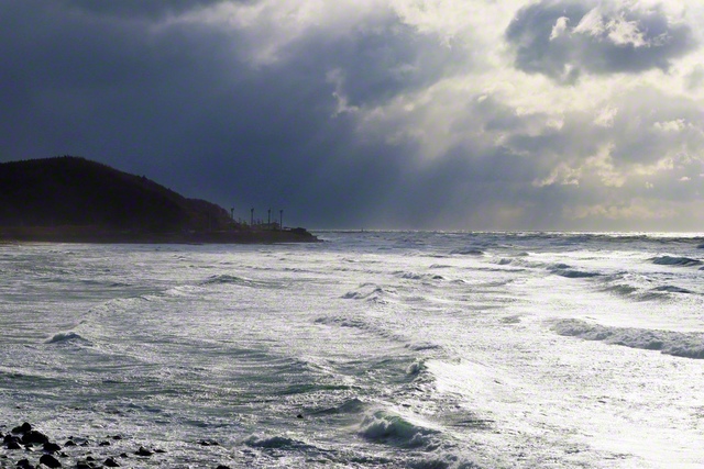 光芒（こうぼう）に照らされる日本海。奥には遊佐風力発電所が