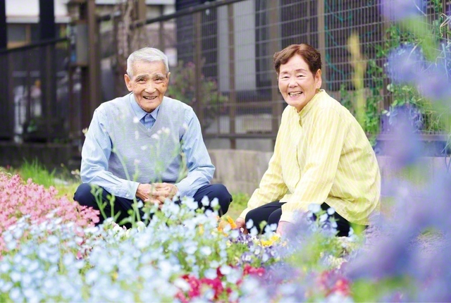 小山さん㊧と妻・文子さん（圏女性部主事）は、共に広布に駆けてきた戦友。文子さんも乳がんや狭心症を患ったが、信心根本に乗り越えた。長年、隣人に請われて近所の土地で花や野菜を夫妻で育て、近隣の人たちの憩いの場になっている。自然と友好の輪も広がり、多くの人が聖教新聞を購読してくれている