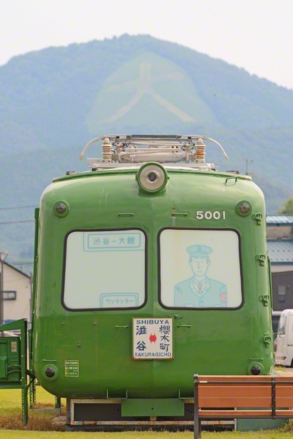 鳳凰山に浮かぶ大文字を背景にたたずむ青ガエル。「渋谷-大館」の行き先表示が、遠く離れた二つの町をつないでいるようだった