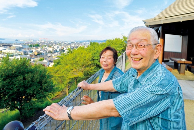 経済的に苦しかった時、坪井さん㊨は同志のためにと個人会場を新築。今も現役の美容師として働く妻・ケイ子さん（女性部副本部長）は心を決めるため弘教に走り、会場を建てた年に6人が入会した。住宅ローンを完済した今、坪井さんは「妻には頭が上がりません」と。夫妻は4人の子を育て上げ、多くの孫やひ孫の笑顔に囲まれている